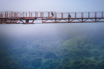 Workers maintaining a swaying (or suspension) bridge on a foggy morning. Hantan River, Gangwon-Do, South Korea.