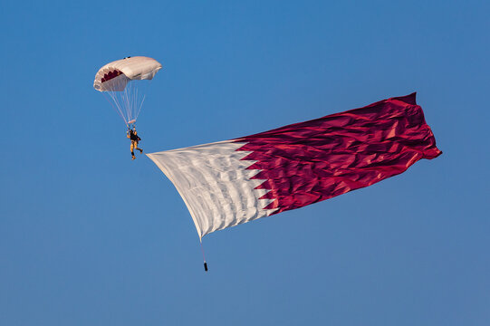 Doha, Qatar &ndash; Skydiving performance by the Lekhwiya Forces team during the Katara cultural events, with a parachutist carrying a large flag attached to the leg while descending through the sky &ndash; stock
