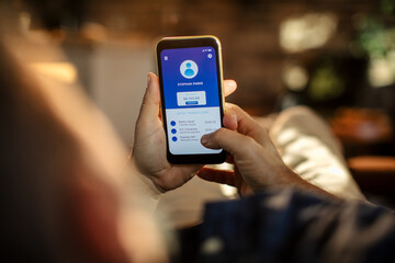 Young man using a banking app on his smart phone while lying down on a couch in the living room