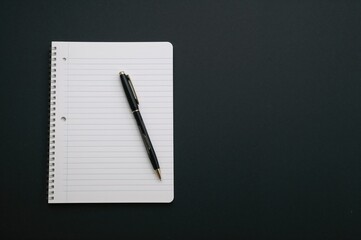 White notebook with horizontal lines and a black pen on a dark textured surface, top-down perspective with copy space