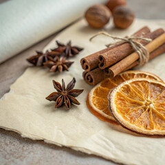 Fototapeta premium Dried orange slices, cinnamon sticks tied with twine, and star anise create a warm and inviting autumnal atmosphere on a textured background, perfect for evoking the scents and feelings of fall