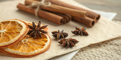 Fototapeta premium Dried orange slices, cinnamon sticks tied with twine, and star anise create a warm and inviting autumnal atmosphere on a textured background, perfect for evoking the scents and feelings of fall