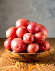 A wooden bowl overflowing with plump, vibrant red potatoes sits on a rustic wooden surface.