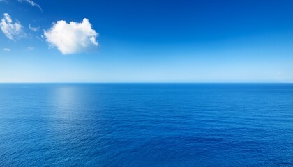 Fototapeta premium a vast expanse of calm blue ocean meets a clear bright sky with a single wisp of white cloud