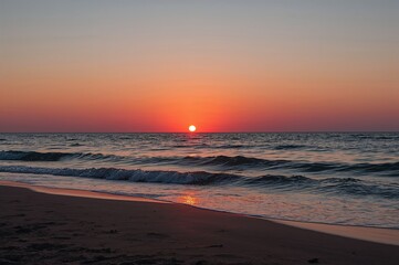 Fototapeta premium Sunset over the shore with vibrant orange, red, and pink hues lighting up the sand and sea waves.