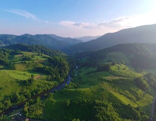 Naklejka premium An aerial view of a valley with rolling hills, lush greenery, and a winding river snaking through the landscape, bathed in soft sunlight.