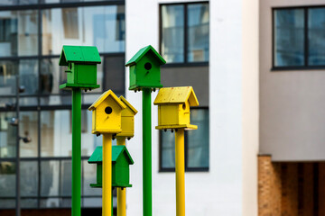 Bright green and yellow birdhouses on long posts against the background of a modern building.