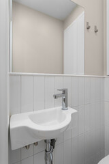 A small white sink with a faucet against a wall with vertical tiles and a mirror.