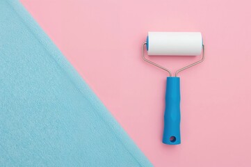 Obraz premium Blue-handled lint roller with paper sheet on a pink backdrop for removing dust, pet hair, and lint from textiles. Space available for text.