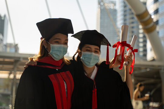 Two women in graduation gowns are wearing masks. Concept of formality and seriousness, as the women are dressed in their graduation attire and wearing masks.