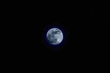 Obraz premium Blue supermoon glowing with blue halo and starry aura in dark night sky