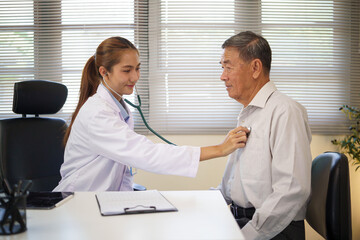 Young female doctor examining an elderly man heartbeat with a stethoscope in a modern medical...