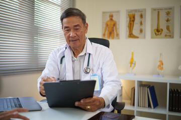Experienced male doctor n white coat filling out patient records in a bright clinic with anatomical charts.