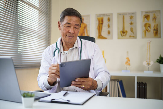 Senior male doctor uses a digital tablet for reviewing medical data or conducting virtual consultations in a clinic