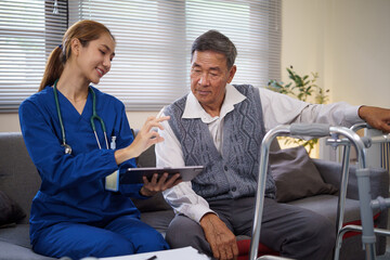Female nurse in blue scrubs shows medical information to senior man on a digital tablet during a home care visit.