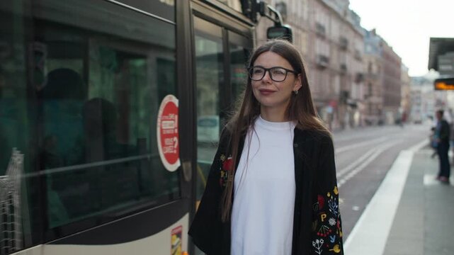 A woman stands at a bus stop and a city bus passes by her. Urban transport moves in a metropolis.