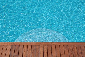 Obraz premium Contemporary fiberglass pool stairs leading into clear, cool blue water under a sunny sky in a garden or hotel spa setting with a teak wood deck.