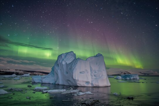 Glowing green auroras above a nighttime iceberg drifting in a remote waterway - Powered by Adobe