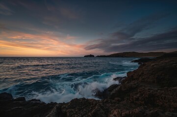 Obraz premium Gloomy coastal scene featuring rugged shoreline and vibrant sunset hues