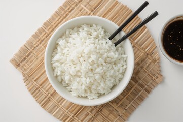 Steamed organic jasmine basmati rice served in a white dish with dark chopsticks and sweet soy sauce on a bamboo mat against a white backdrop