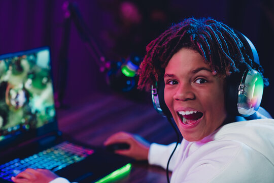 Young male gamer streaming online in a vibrant neon-lit room with a laptop, enjoying a gaming session