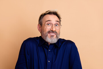 Mature man in blue shirt showing a quirky expression against a beige backdrop, reflecting humor and individuality