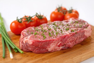 Fototapeta premium Raw beef entrecote steak on a chopping board with fresh chives and cherry tomatoes against a white backdrop