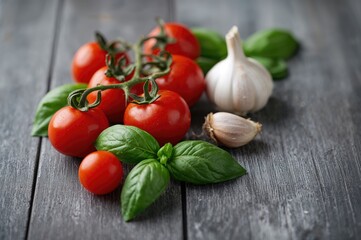 Close-up view of cherry tomatoes, garlic cloves, and fresh basil leaves on a rustic grey wooden surface with ample space for text.
