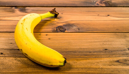 A single ripe banana rests on a rustic wooden surface, showcasing its yellow peel and stem.