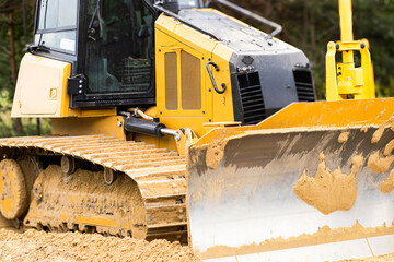 Heavy machinery bulldozer with yellow and black exterior is parked on a construction site, showcasing powerful tracks and blade, ready for earth-moving tasks
