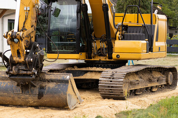 Yellow excavator with a large bucket is parked on a construction site, surrounded by sand and grass, showcasing heavy machinery in action and construction environment