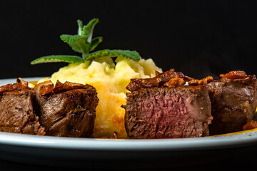 Filet mignon with fried onion and mashed potato, decorated with cherry tomatoes and mustard sauce on black background.
