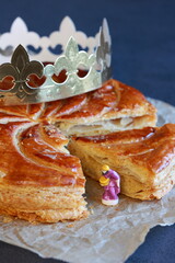 Galette des rois with a golden crown and figurine of king stands out on dark vertical background 