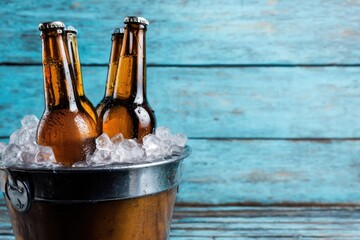 Cold beer bottles in ice bucket against blue wooden background, perfect for party invitations, summer celebrations, bar advertising and festive drink designs