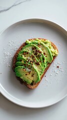 Avocado toast with chili flakes and salt on a white plate.