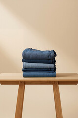 Folded Denim jeans stack on wooden table. Minimal studio scene with neutral beige background and copy space. Clean fashion apparel product photography. Modern retail banner.