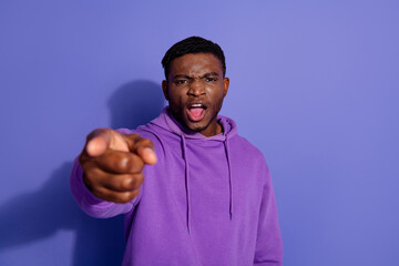 Young stylish man in a purple hoodie pointing forward, emphasizing determination against a vivid violet background