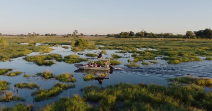Aerial panning. Tourists on a sightseeing boat on a river in the Okavango Delta at sunset