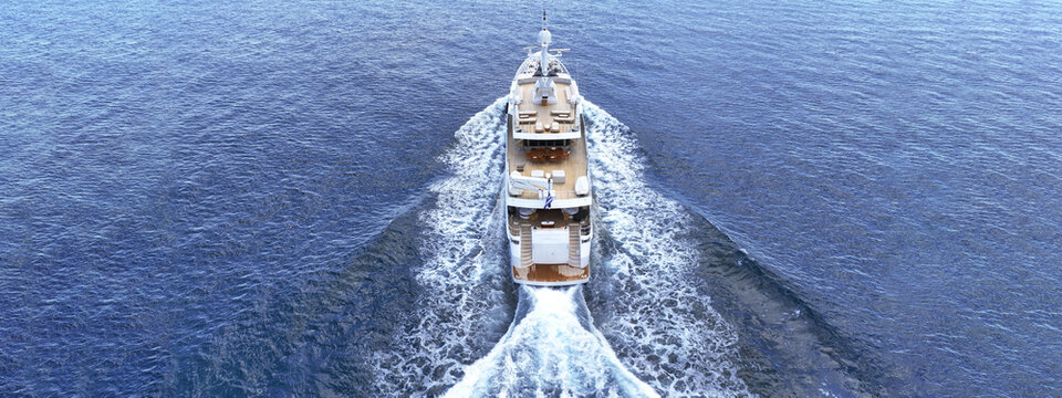 Aerial drone ultra wide tracking photo with copy space of beautiful modern super yacht with wooden deck cruising in high speed deep blue Aegean sea