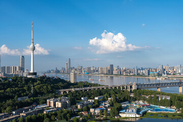 Obraz premium Wuhan Yangtze river China cityscape with a tall tower and bridge under a blue sky with clouds.