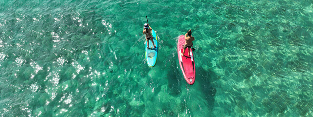 Aerial drone ultra wide photo of couple practice Stand Up Paddle board or SUP surf in tropical exotic island bay with emerald crystal clear sea