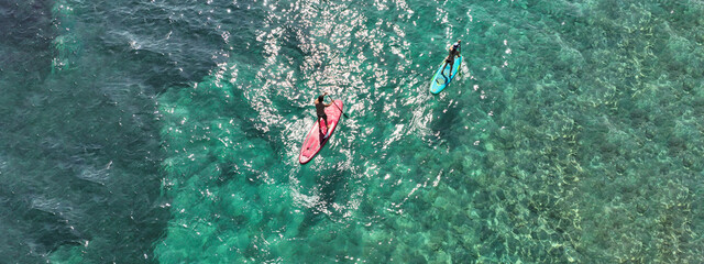 Aerial drone ultra wide photo of couple practice Stand Up Paddle board or SUP surf in tropical exotic island bay with emerald crystal clear sea