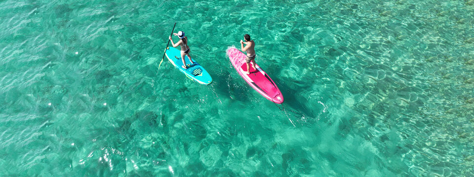 Aerial drone ultra wide photo of couple practice Stand Up Paddle board or SUP surf in tropical exotic island bay with emerald crystal clear sea