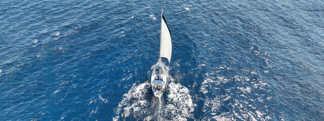 Aerial drone ultra wide tracking photo with copy space of beautiful sail boat with trained crew cruising in deep blue Aegean sea
