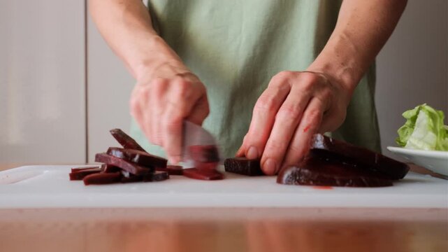 Closeup of an adult woman slicing beetroot on a cutting board at a home kitchen counter.