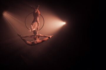 Duo aerial hoop performance with two female acrobats. One hangs upside down from the hoop,...