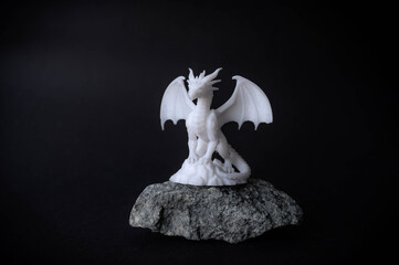 Detailed white dragon miniature with spread wings, placed on a rough stone surface against a black background, fantasy and mythical creature concept.