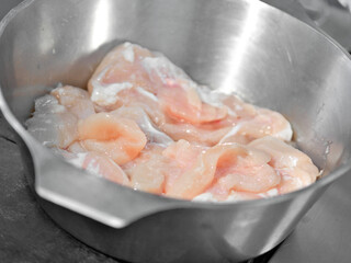 Raw chicken pieces in steel pot for cooking preparation.