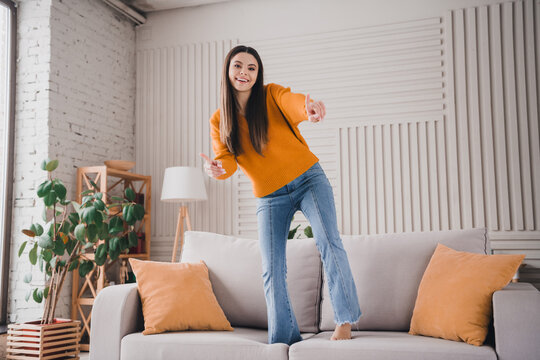 Cheerful girl in a cozy living room wearing casual attire, standing joyfully on a gray couch, enjoying the relaxed and vibrant atmosphere - Powered by Adobe