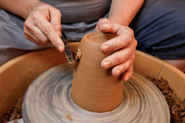 Unrecognisable woman's hands working on a potter's wheel with traditional tools in a workshop. Small business concept.